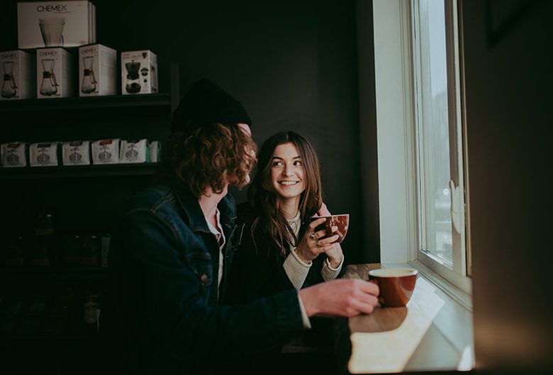 Man and woman drinking coffee by a window.