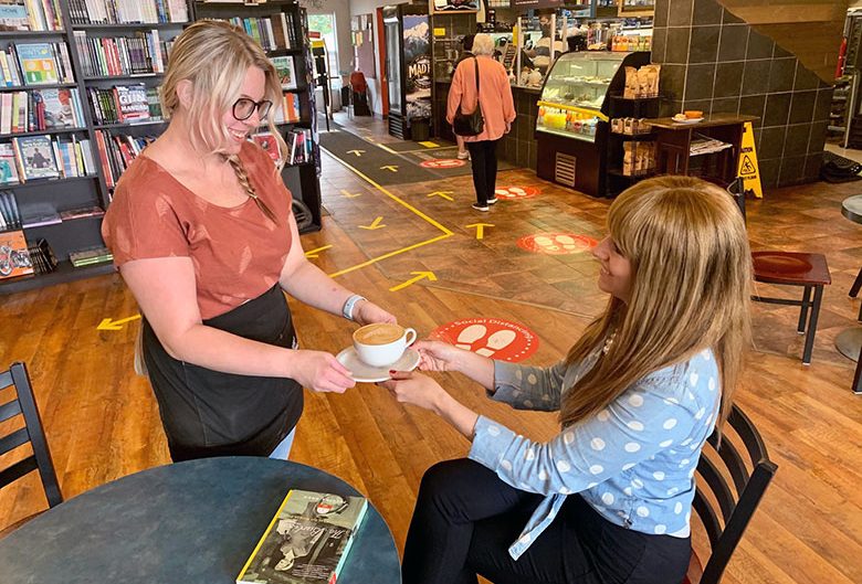 Woman handing another woman a coffee.