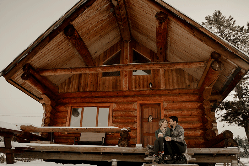 Couple sitting in front of cabin in winter.